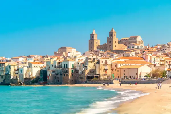 La costa di Cefalù con le sue case colorate e il mare azzurro. La cattedrale domina il panorama.