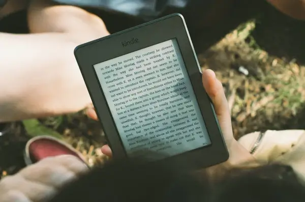 Une personne lit un livre sur une liseuse, profitant du soleil. L'encre numérique offre une lecture confortable en extérieur.
