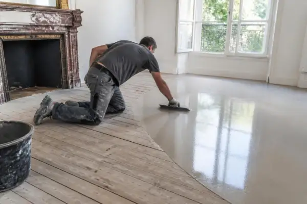 Un ouvrier effectue un ragréage sur plancher bois, créant une surface lisse et moderne.