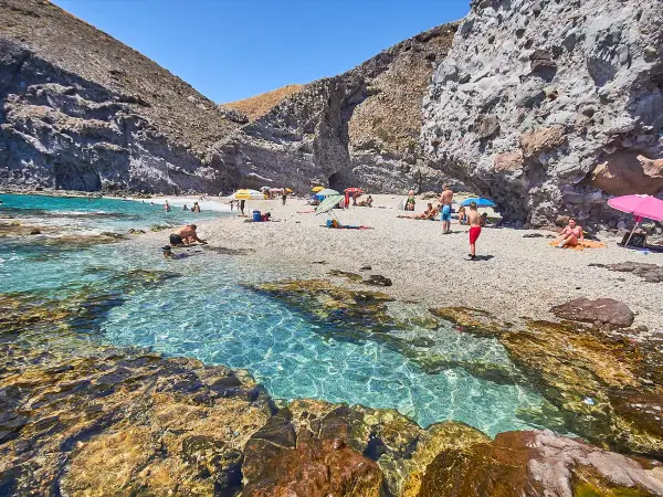 Descubre qué ver en Carboneras: una cala rocosa con aguas cristalinas y gente disfrutando del sol y el mar.