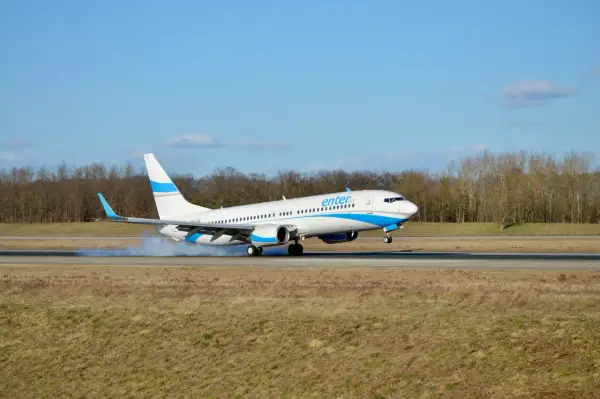 Samolot Enter Air ląduje, koła dotykają pasa, unosząc pył.