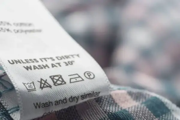 Metka z instrukcją prania: prać w 30°C, nie wybielać, prasować w niskiej temperaturze, czyścić chemicznie. Nazwy materiałów: bawełna, poliester.