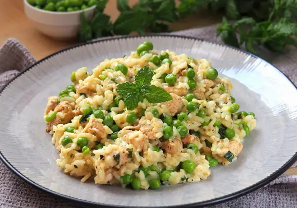 Pyszne risotto z groszkiem i kawałkami kurczaka, udekorowane listkiem mięty. Idealne na lekki obiad.
