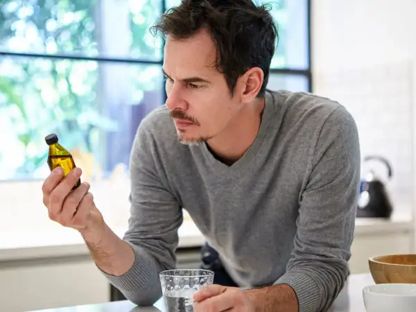 Uomo pensieroso guarda una fiala di liquido giallo, chiedendosi se la vitamina B12 fa ingrassare.