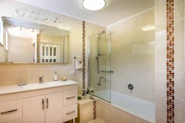 Baño moderno con ducha y bañera, lavabo con mueble y espejo decorado con un lagarto. El alicatar baño resalta con detalles en mosaico.