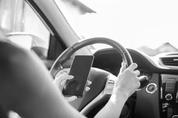 Une main tient un téléphone au volant, distrayant le conducteur. Une conduite dangereuse qui peut coûter 6 points sur le permis.