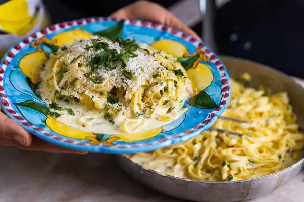 En tallrik med krämig pasta al limone, toppad med parmesan och persilja, serveras från en panna.