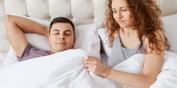 Kobieta z zaciekawieniem patrzy na śpiącego mężczyznę, zastanawiając się, dlaczego penis staje.