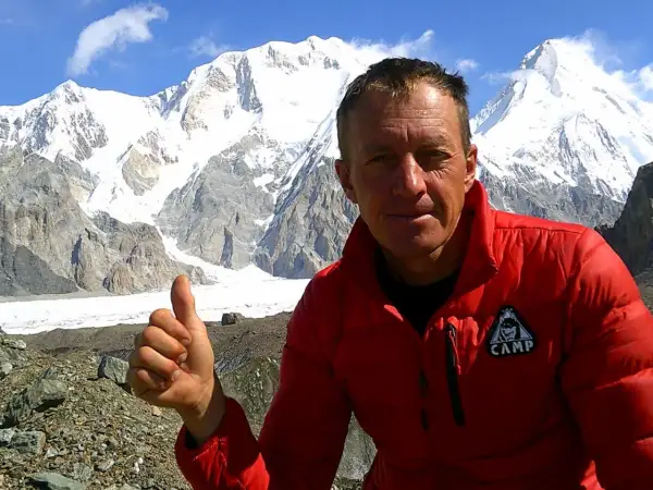 Bergsteiger Denis Urubko gibt Daumen hoch vor schneebedeckten Gipfeln.