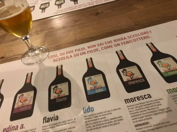 Un bicchiere di birra e un menu del birrificio Rubiu con diverse etichette di birra.