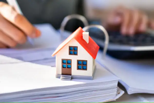 Hausmodell auf Dokumenten, Hände schreiben und tippen. Berechnung der Hessen Grunderwerbsteuer für den Hauskauf.