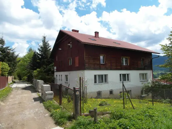 Stacja turystyczna Abrahamów, drewniano-betonowy budynek z czerwoną dachem, otoczony zielenią i polnymi kwiatami.