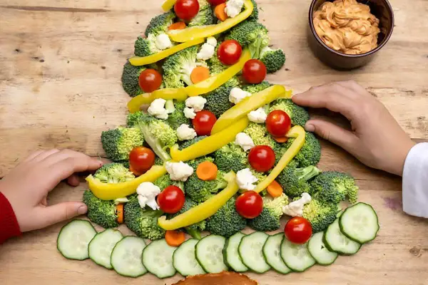 Une joyeuse planche apéritif noël en forme de sapin, décorée de brocolis, tomates cerises, poivrons jaunes, chou-fleur et rondelles de concombre.