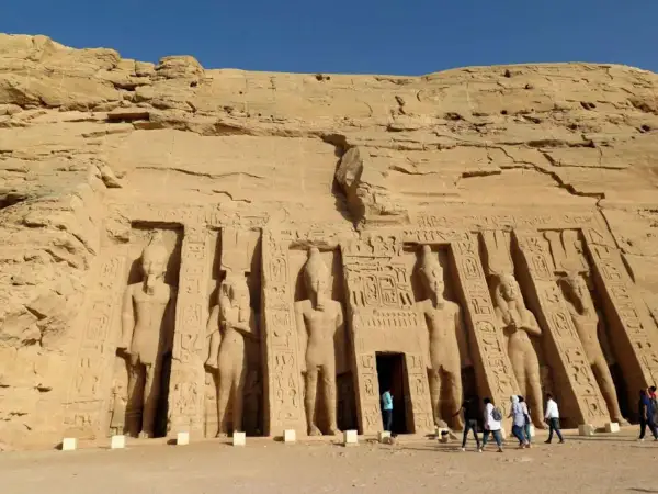 Gigantescas estatuas talladas en la roca flanquean la entrada del templo de Abu Simbel. Turistas admiran la majestuosidad de este sitio histórico.