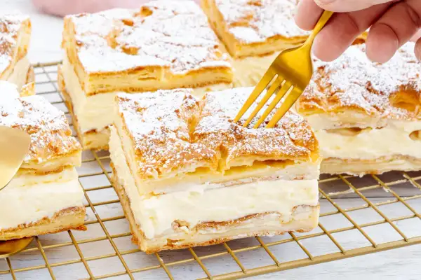 Ein goldener Löffel sticht in ein Stück polnischer Puddingkuchen, bestäubt mit Puderzucker.