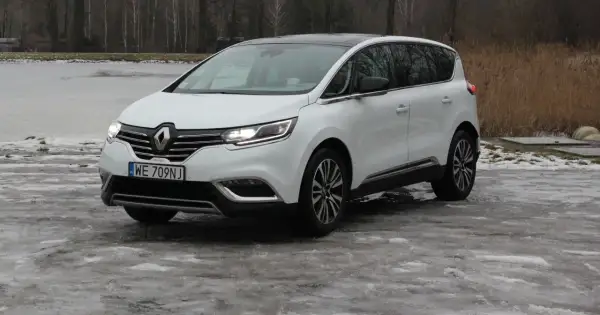 Biały Renault Initiale na oblodzonym podjeździe, z widokiem na zamarznięte jezioro i drzewa.
