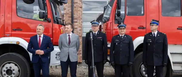 Uroczystość przed remizą OSP. W garniturach i mundurach strażackich stoją mężczyźni, wśród nich zastępca naczelnika OSP.