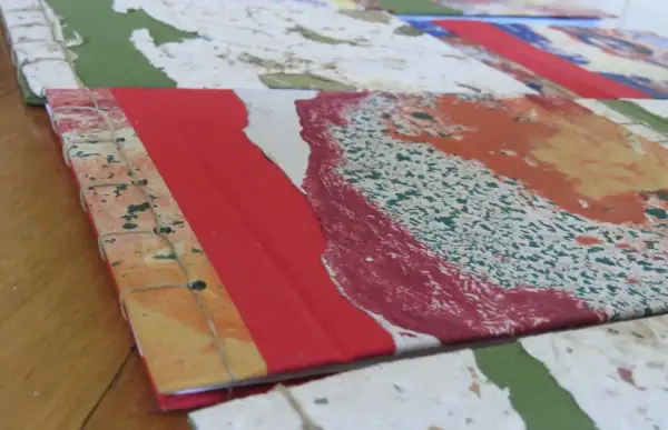 Dettaglio di come rilegare fogli a mano con filo, creando un quaderno artistico con copertina colorata.