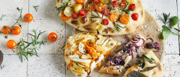 Zwei Focaccias mit Tomaten, Gemüse und Zwiebeln, garniert mit Rosmarin und Salbei.