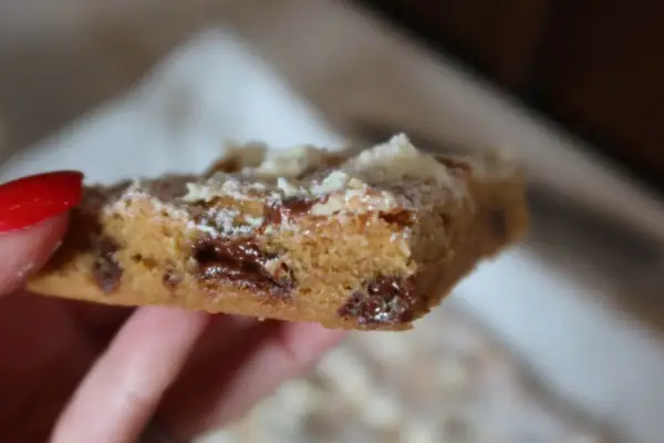 En hand håller en bit av ett blondie recept med chokladbitar.