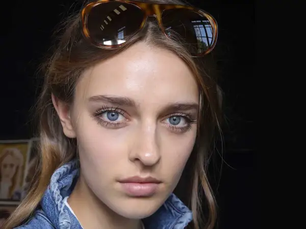 Ragazza con occhiali da sole in testa, viso illuminato da fondotinta e fard, ciglia lunghe e occhi azzurri.