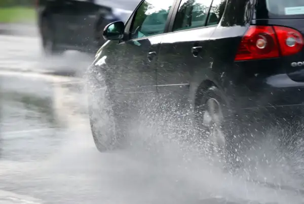 Un coche negro salpica agua al pasar por un charco. En días de lluvia, una distancia de frenado segura depende de la precaución.