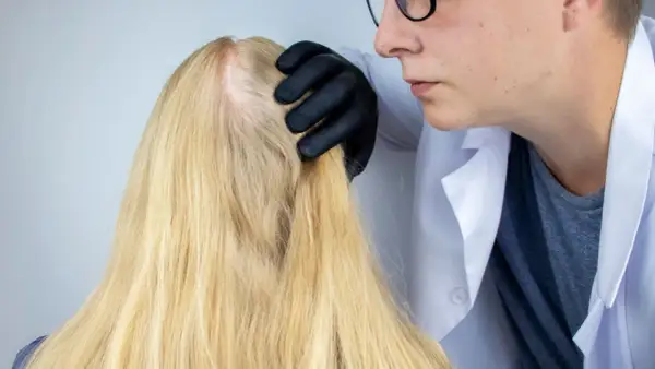 Lekarz od włosów w czarnej rękawiczce bada blond włosy pacjentki, oceniając ich kondycję.