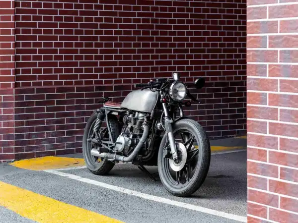 Stylowy motocykl miejski z metalicznym bakiem i brązowym siedzeniem stoi przy ceglanej ścianie.