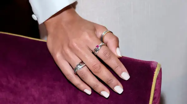 Mano con varios anillos, uno de ellos en el dedo anular con una piedra rosa.