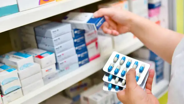 Ręka farmaceuty wybiera z półki lek, w tym antybiotyk azytromycyna w blistrach.