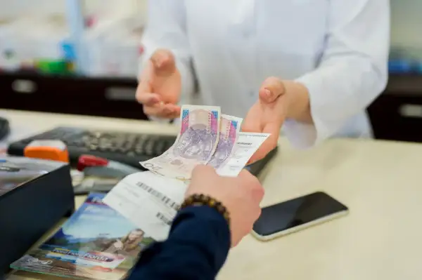 Dłoń podaje farmaceucie polskie banknoty i receptę.