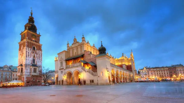 Wieczorny rynek główny Kraków. Sukiennice i wieża ratuszowa oświetlone, niebo granatowe.