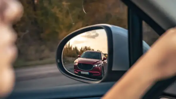 Reflejo de un coche rojo en el espejo retrovisor, preparándose para un adelantamiento. DGT.