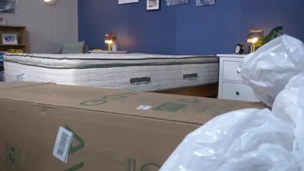 A mattress that expands when opened is shown, partially covered by a cardboard box and plastic packaging.