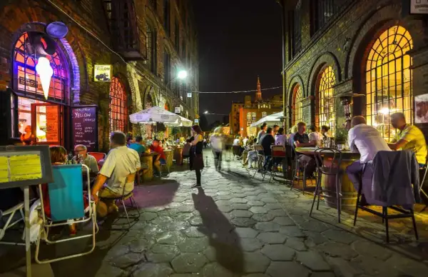Wieczór na ul. Piotrkowskiej w Łodzi. Ludzie siedzą przy stolikach w restauracjach, ciesząc się atmosferą.