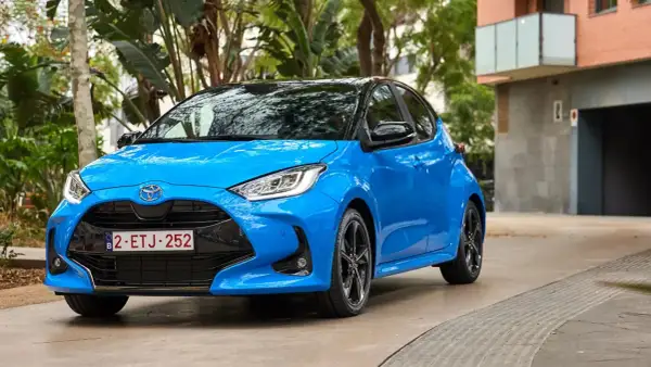 Błękitna Toyota Yaris 1.3 benzyna zaparkowana na tle zieleni i budynku. Zastanawiasz się, jaki olej do toyoty yaris 1.3 benzyna?