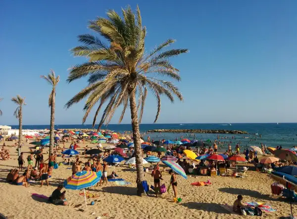 Spiagge Marina di Ragusa affollate di bagnanti sotto palme e ombrelloni colorati, con il mare azzurro sullo sfondo.