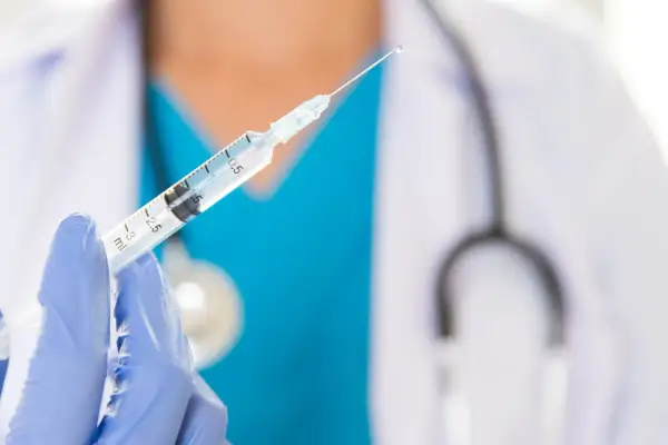 Lekarz w niebieskiej rękawiczce trzyma strzykawkę z kroplą szczepionki. Dostępne są szczepienia na Sri Lance.