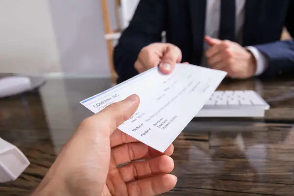 Mancata riscossione di assegno bancario dopo rogito notarile. Mano che porge un assegno, con un uomo in giacca e cravatta sullo sfondo.