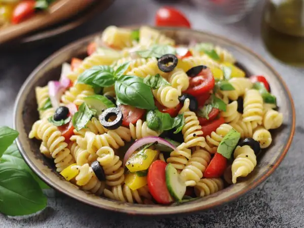 Pasta fredda con pomodorini, olive, basilico e cipolla rossa. Perfetta per ricette pasta fredda veloci e sfiziose.
