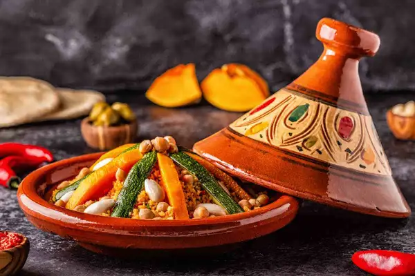 Un saporito cous cous tajine con verdure colorate e ceci, servito in un tradizionale piatto di terracotta decorato.