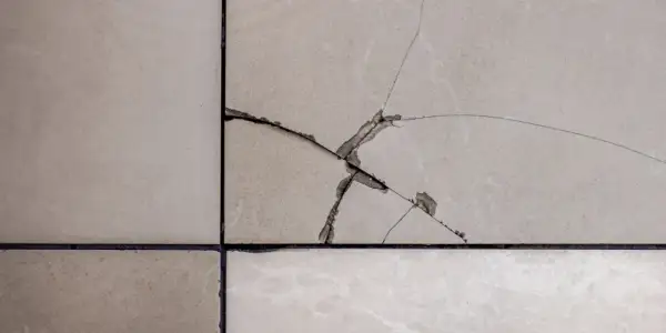 Gros plan sur un carrelage beige avec une fissure traversant plusieurs carreaux, révélant la couche inférieure.