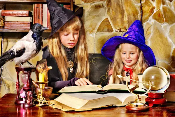 Dwie dziewczynki w strojach czarownic tworzą magiczne prace plastyczne na Andrzejki, otoczone tajemniczymi rekwizytami.
