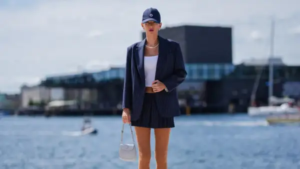 Ein gestreifter, **blauer Blazer kombiniert** mit einem kurzen Rock und weißem Top. Eine Frau trägt das Outfit am Wasser.