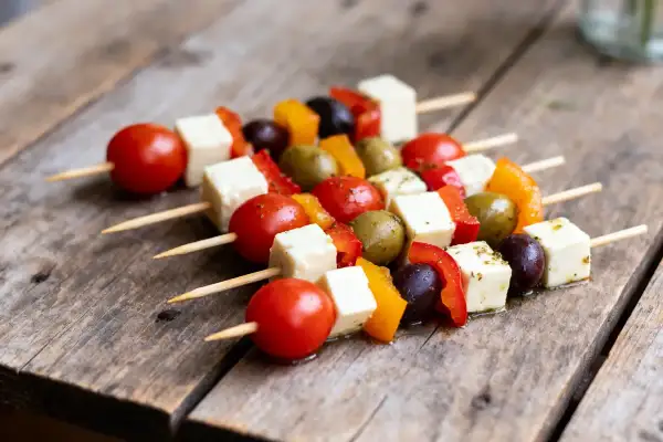 Des brochettes apéro colorées avec des tomates cerises, des cubes de fromage, des poivrons et des olives sur une table en bois.