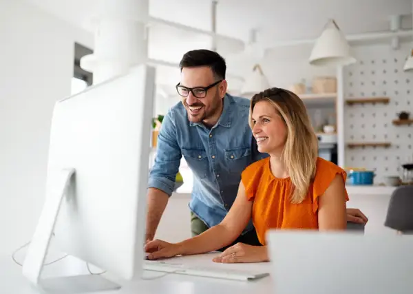 Coppia sorridente davanti al computer, scopre come funziona la banca ore per ottimizzare il lavoro.