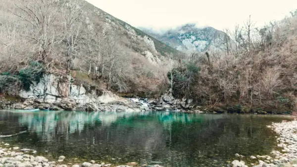 El río turquesa fluye sereno, reflejando árboles desnudos y montañas neblinosas. Un paisaje que evoca la paz de la olla de San Vicente.