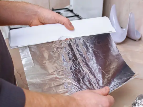 Dłoń trzyma folię aluminiową z dozownika. Błyszcząca strona folii utrzymuje ciepło, idealna do pieczenia.