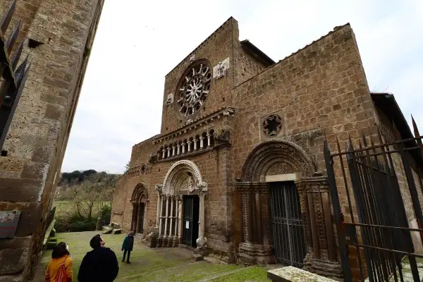 La facciata romanica di Santa Maria Maggiore a Tuscania, con il suo rosone e i portali scolpiti, vista da un angolo con visitatori che ammirano la struttura.