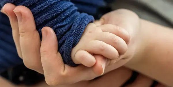 Eine Hand hält zart die kleine Hand eines Babys. Die Frage, warum hilft Gott nicht bei Depressionen, hallt in dieser Geste der Verbundenheit wider.